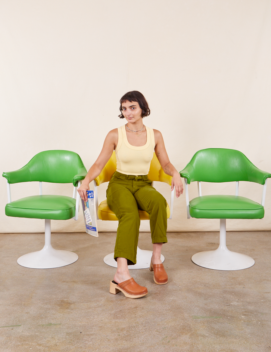 Soraya is sitting in a yellow chair wearing Work Pants in Olive Green and a butter yellow Tank Top