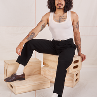 Jesse is sitting on a stack of wooden crates. They are wearing Denim Trouser Jeans in Black and a vintage off-white Tank Top