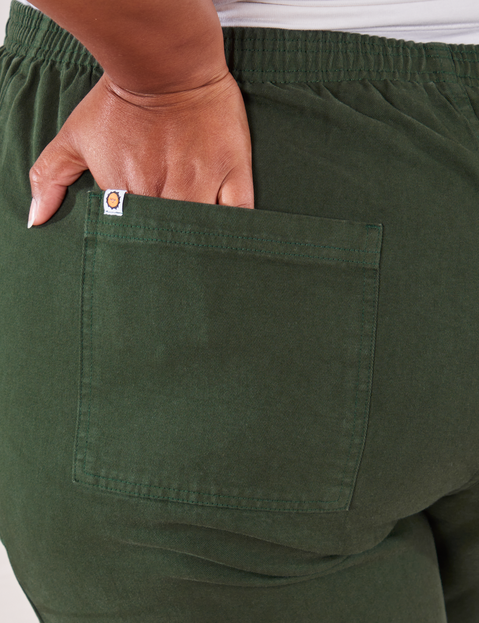 Action Pants in Swamp Green back pocket close up. Morgan has her hand tucked into the pocket.