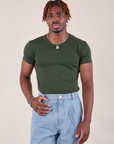 Isaac is wearing Baby Tee in Swamp Green tucked into light wash Denim Trousers