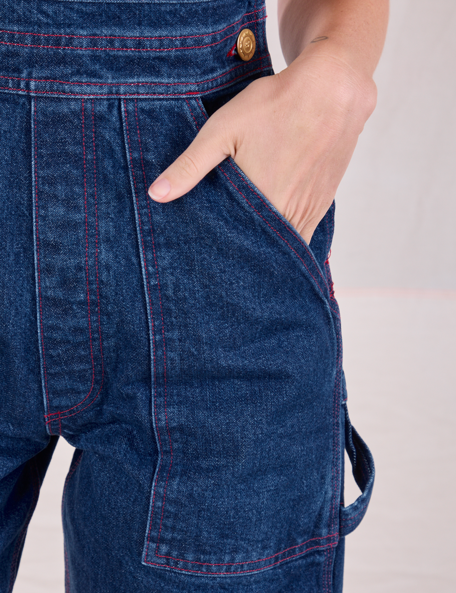 Close up of Alex&#39;s hand in the front pocket of Carpenter Overalls in Dark Wash