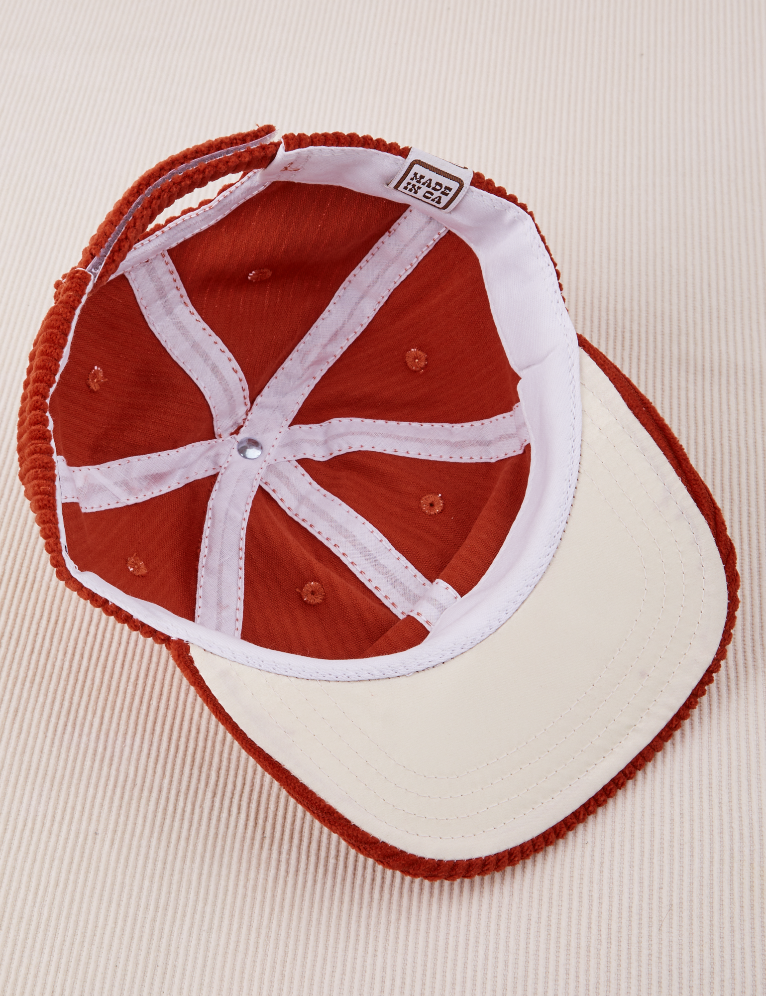 Dugout Corduroy Hat in Paprika flipped over. White satin under-bill.