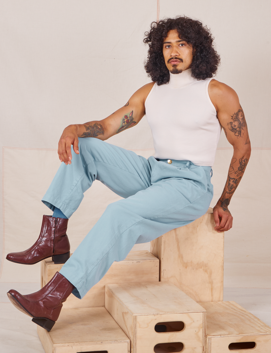Jesse is sitting on a wooden crate wearing Heavyweight Trousers in Baby Blue and vintage off-white Sleeveless Turtleneck