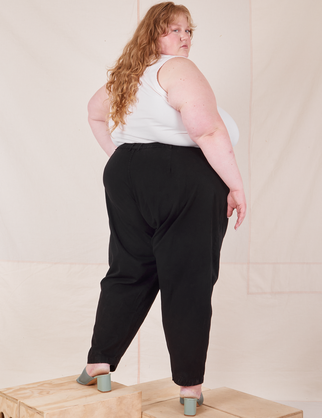 Angled back view of Heavyweight Trousers in Basic Black and vintage off-white Cropped Tank Top worn by Catie