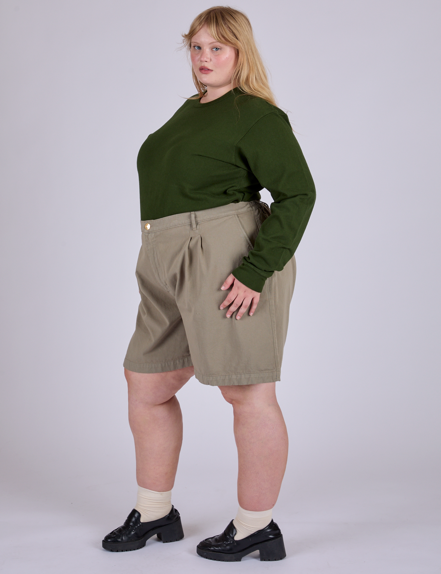 Angled front view of Pleated Trouser Shorts in Khaki Grey and evergreen Long Sleeve Burly Tee on Juliet