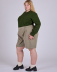 Angled front view of Pleated Trouser Shorts in Khaki Grey and evergreen Long Sleeve Burly Tee on Juliet