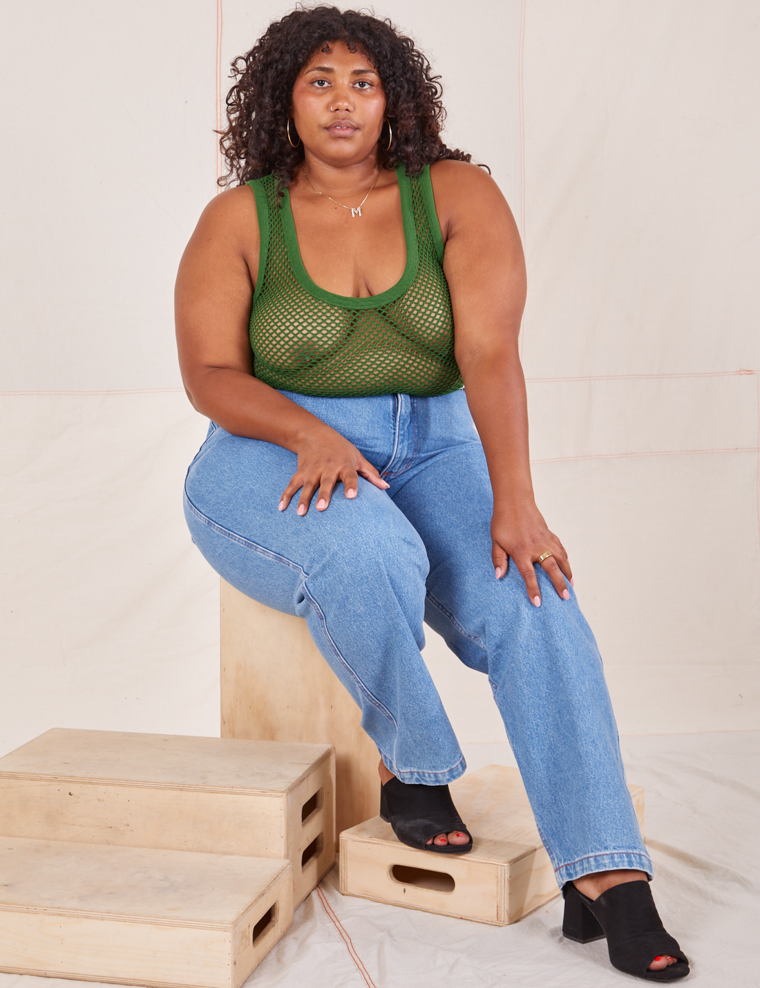 Morgan is sitting on a wooden crate wearing Mesh Tank Top in Lawn Green and light wash Frontier Jeans