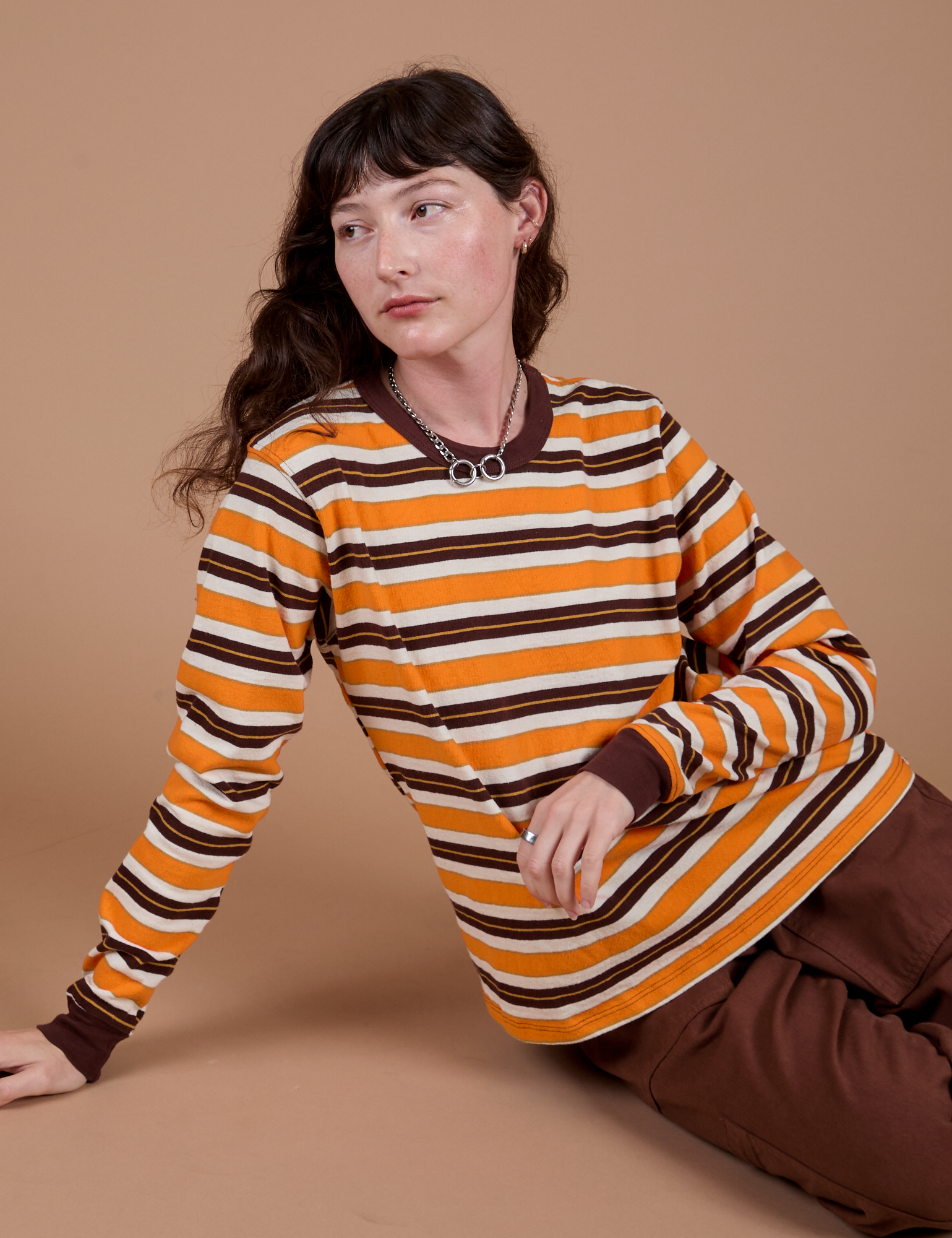 Alex is sitting on the floor and wearing Long Sleeve Striped Burly Tee in Orange