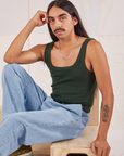 Anthony is wearing Square Neck Tank in Swamp Green and light wash Denim Trousers