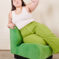 Ashley is sitting on a green upholstered chair wearing Western Pants in Gross Green paired with a vintage off-white Tank Top