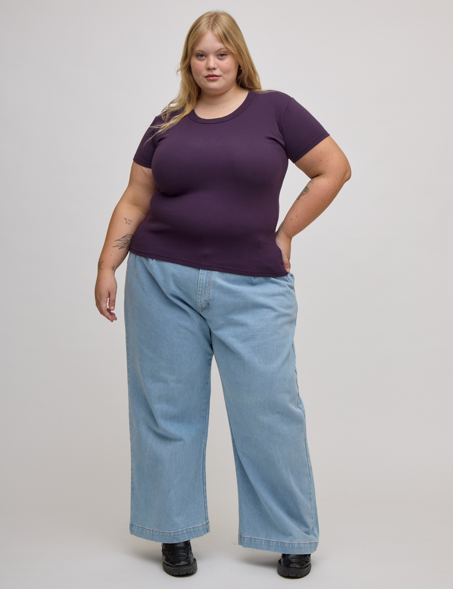 Juliet is wearing Baby Tee in Nebula Purple and light wash denim wide leg trousers