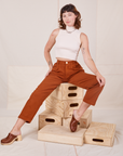Alex is sitting on a stack of wooden crates. She is wearing Heavyweight Trousers in Burnt Terracotta and vintage off-white Sleeveless Turtleneck