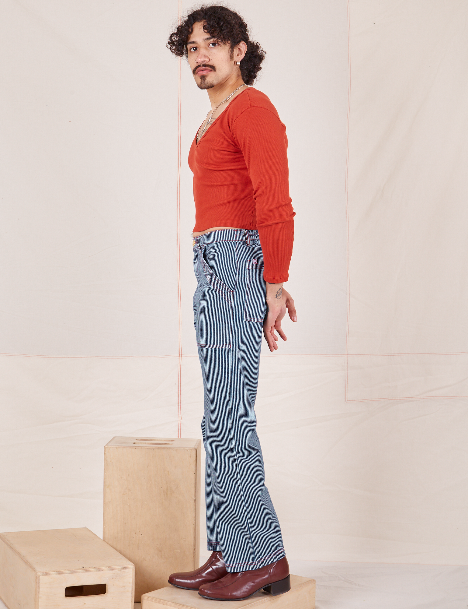 Side view of Railroad Stripe Denim Work Pants and paprika Long Sleeve V-Neck Tee worn by Jesse