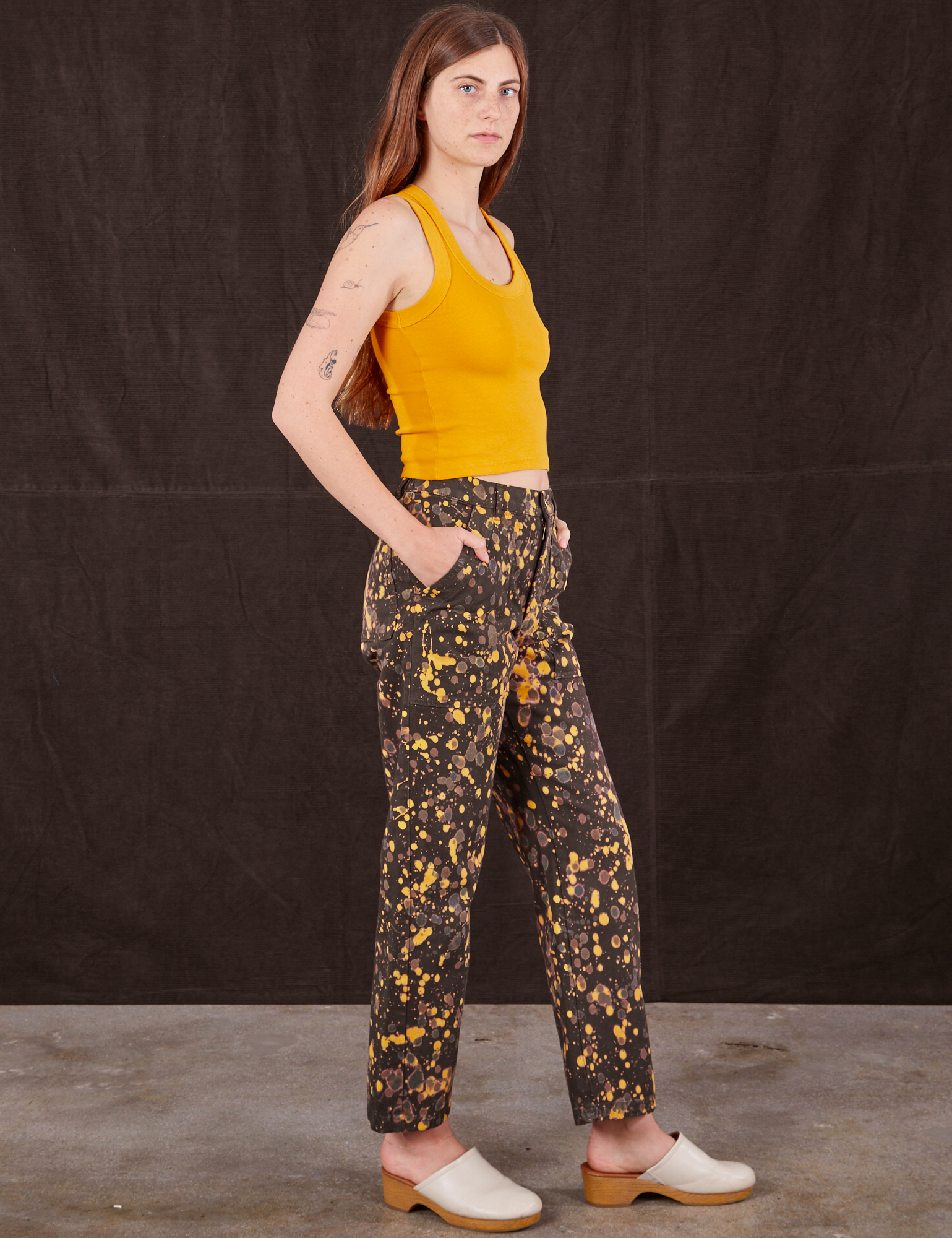 Side view of Marble Splatter Work Pants in Espresso Brown and mustard yellow Tank Top on Scarlett