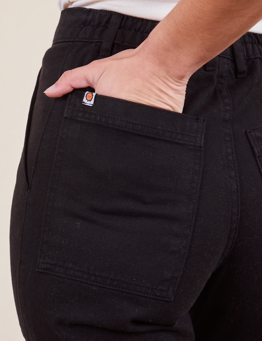 Back pocket close up of Work Pants in Basic Black. Soraya has her hand in the pocket