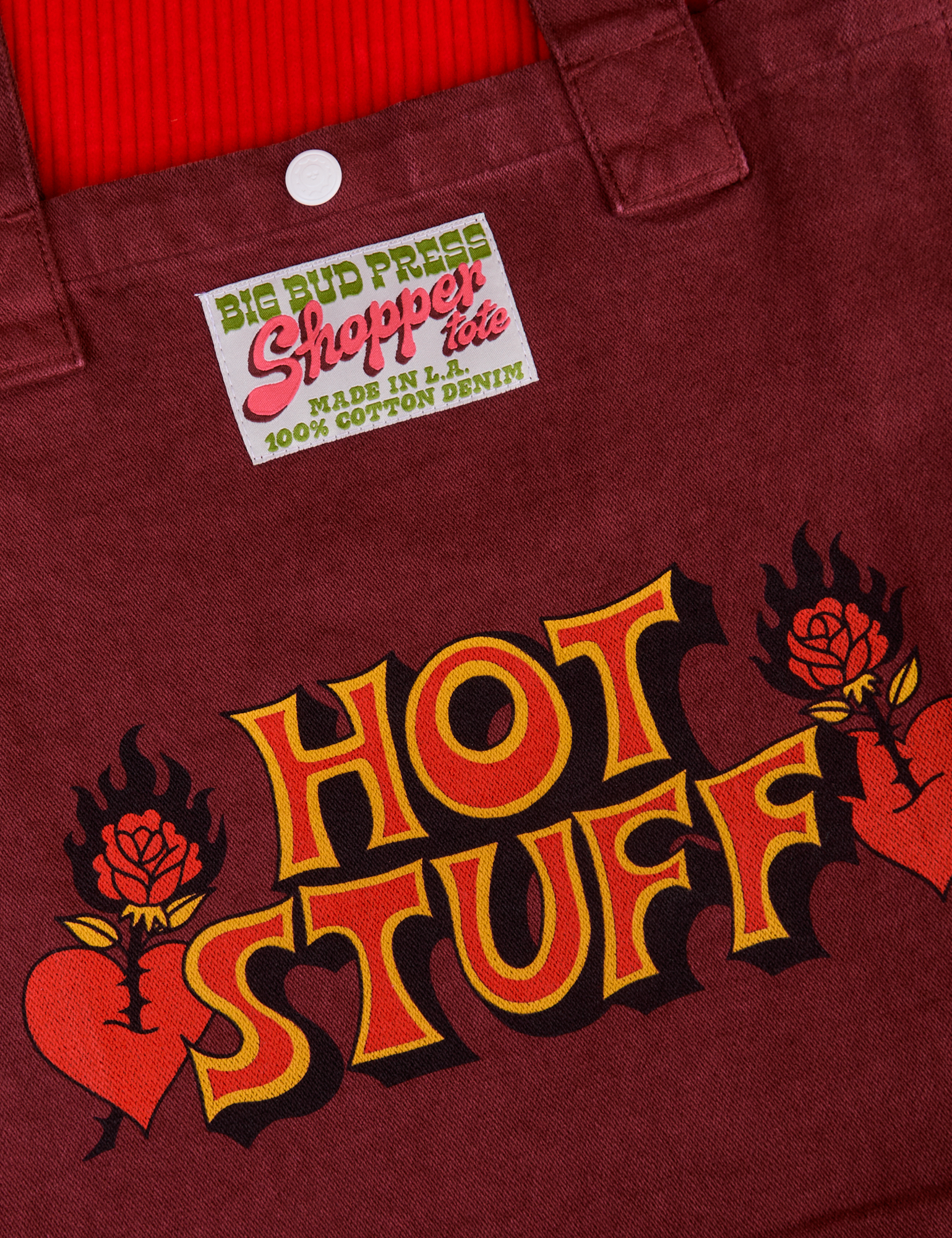 Hot Stuff Shopper Tote close up. Red Hot Stuff Text outlined with yellow. Red heart with rose piercing through on both sides of text.