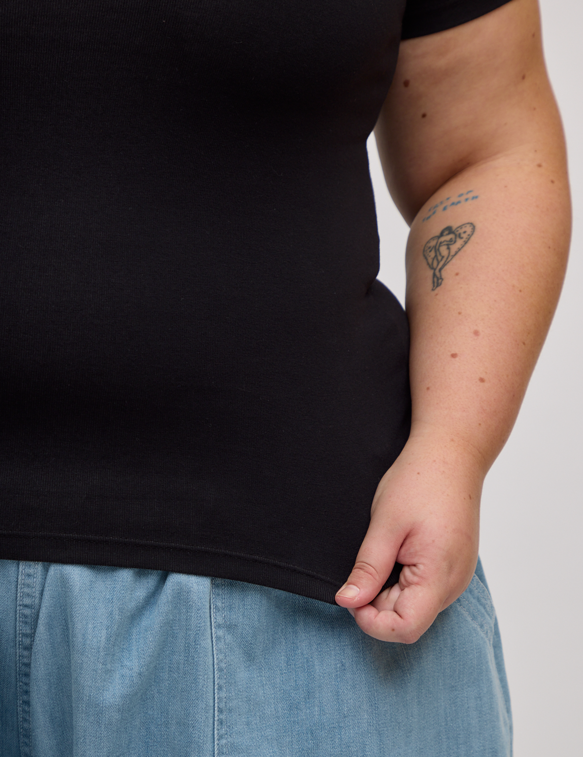 Close up of Juliet holding the bottom hem of Baby Tee in Basic Black