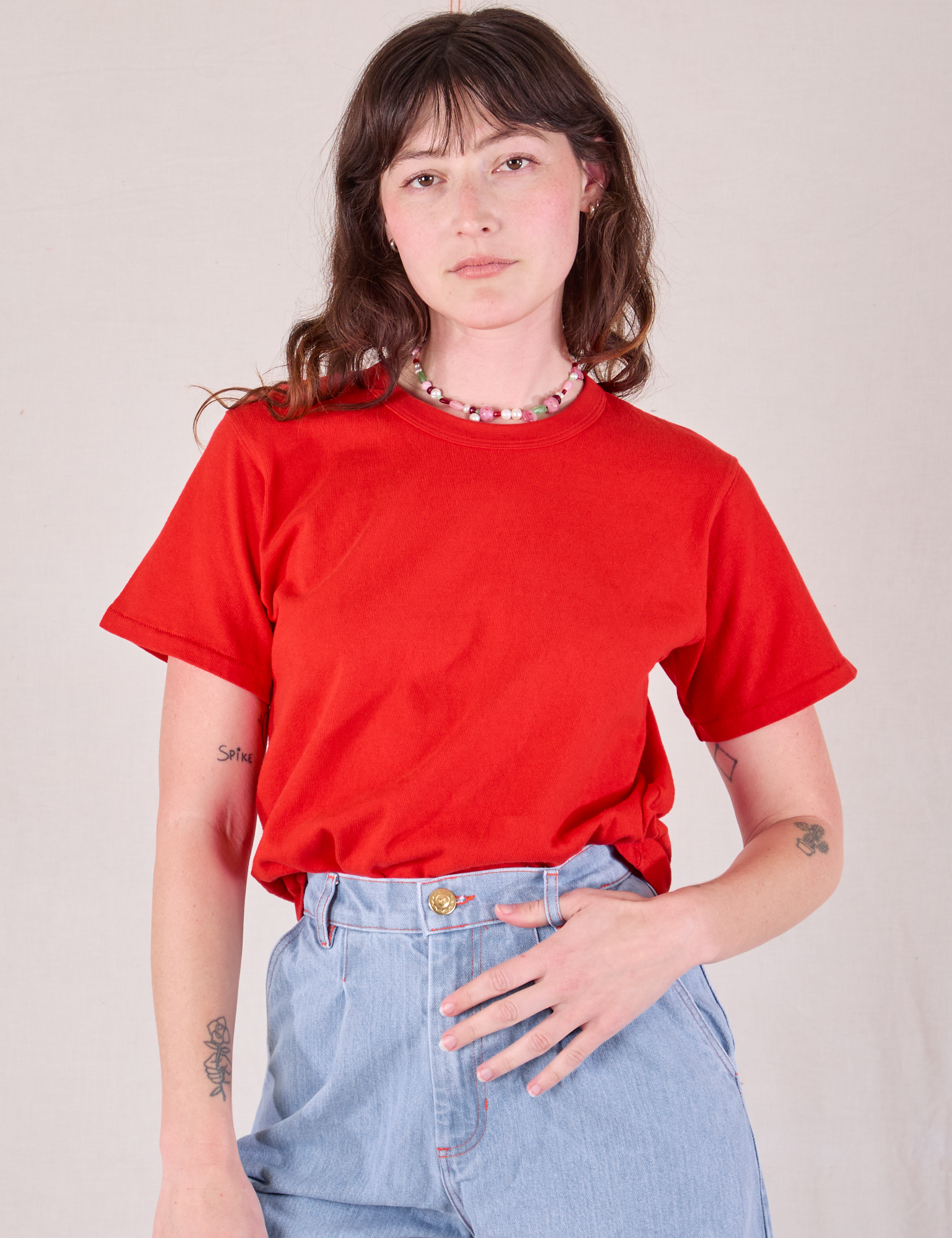 Alex is wearing Burly Tee in Mustang Red tucked into light wash Wide Leg Trousers