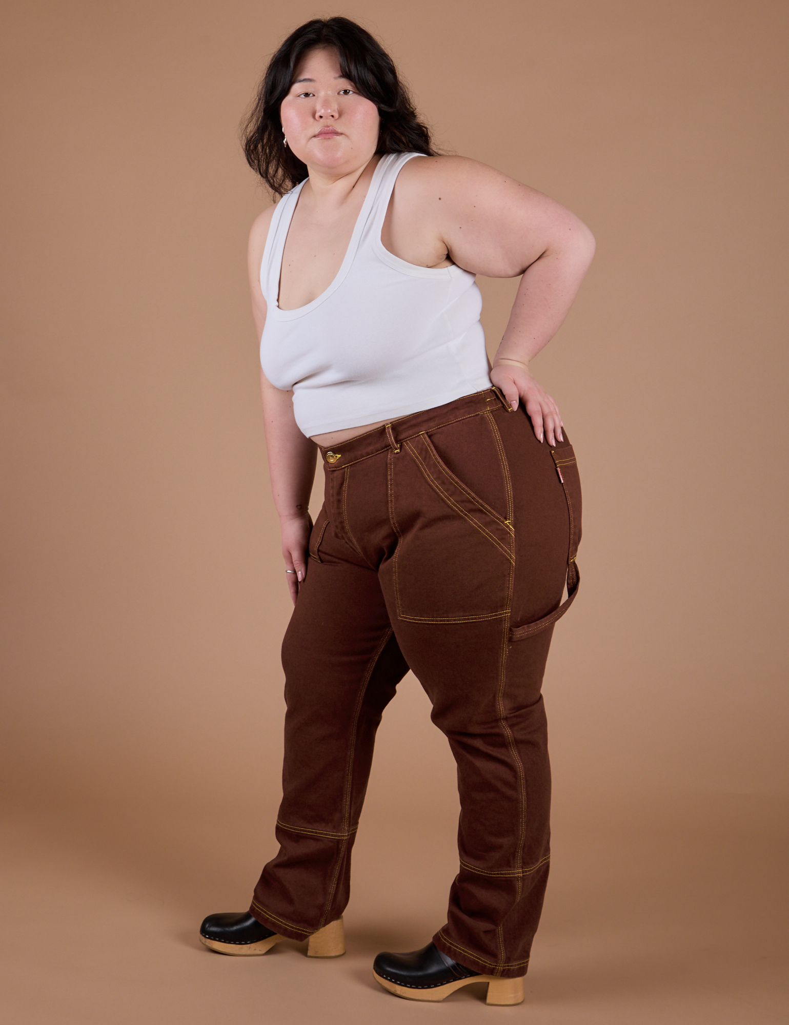 Angled front view of Carpenter Jeans in Fudgesicle Brown and Cropped Tank in Vintage Tee White on Ashley