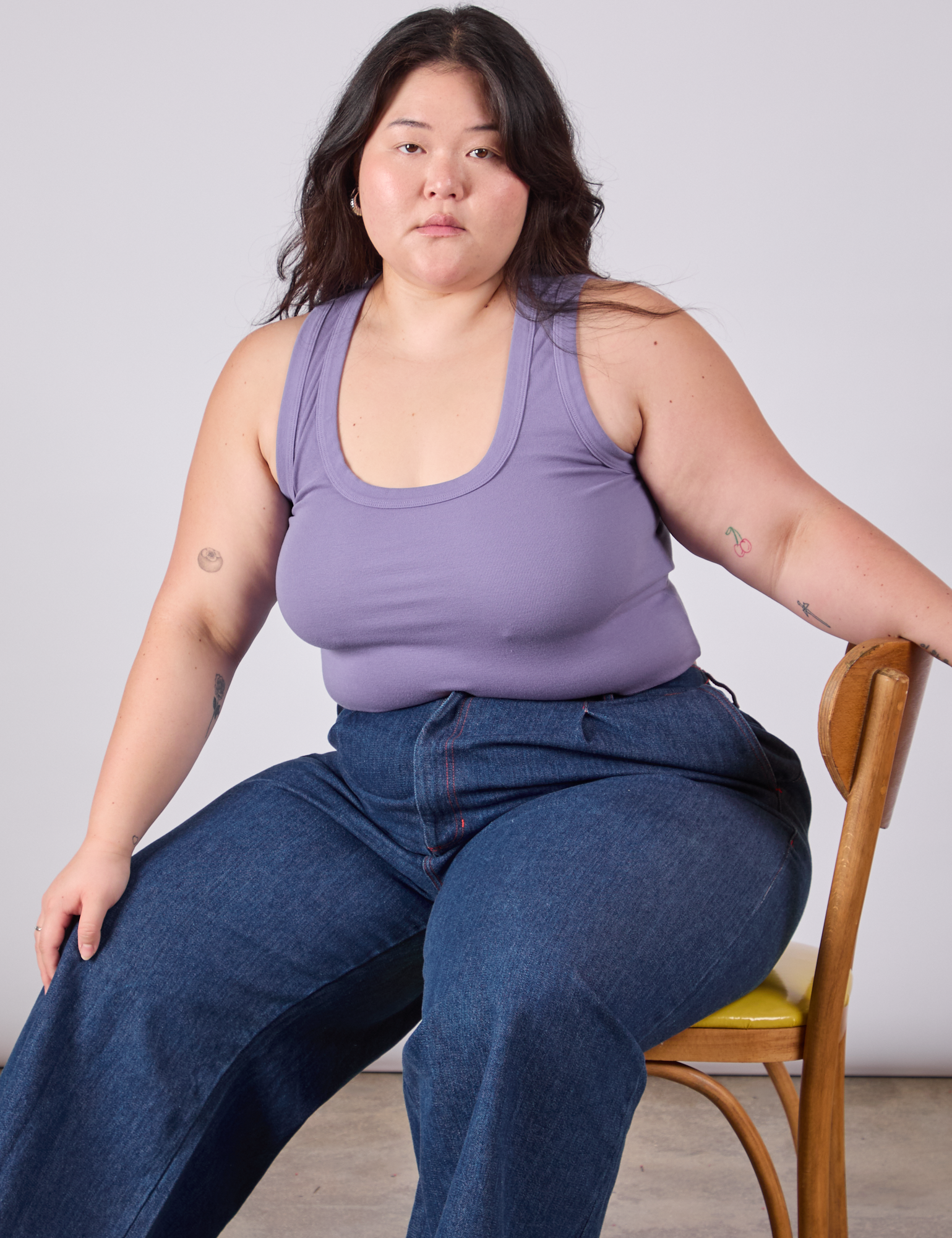 Ashley is sitting in a chair and wearing Cropped Tank Top in Faded Grape paired with dark wash Indigo Wide Leg Trousers