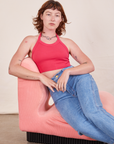 Alex is sitting on a light pink upholstered chair wearing a Halter Top in Hot Pink paired with light wash Frontier Jeans