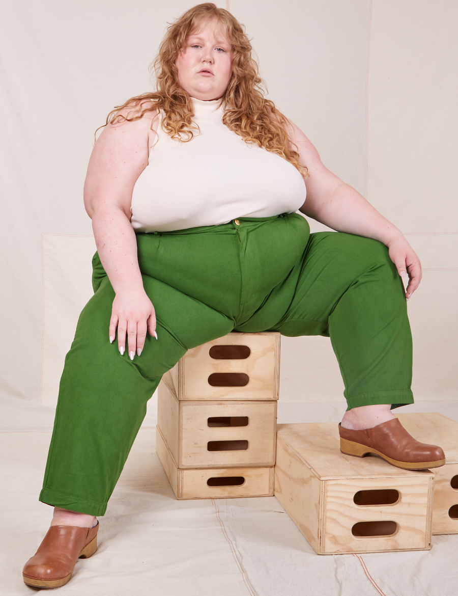 Catie is sitting on a stack of wooden crates. She is wearing Heavyweight Trousers in Lawn Green and vintage off-white Sleeveless Turtleneck.