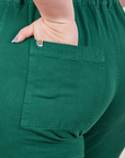 Back pocket close up of Petite Short Sleeve Jumpsuit in Hunter Green. Ashley has her hand in the pocket.