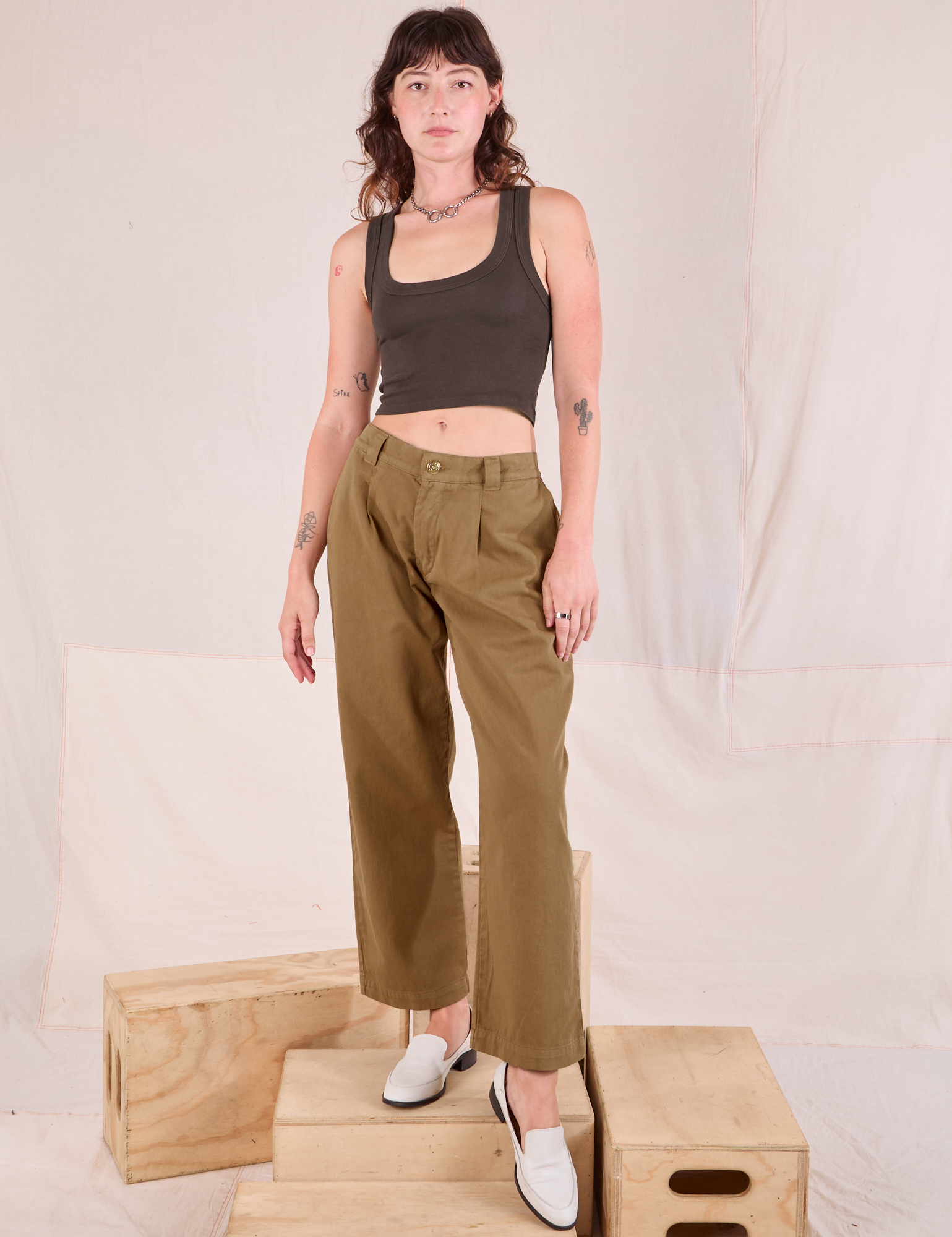 Alex is wearing Mid-Rise Pleated Trousers in Desert Brown and espresso brown Cropped Tank