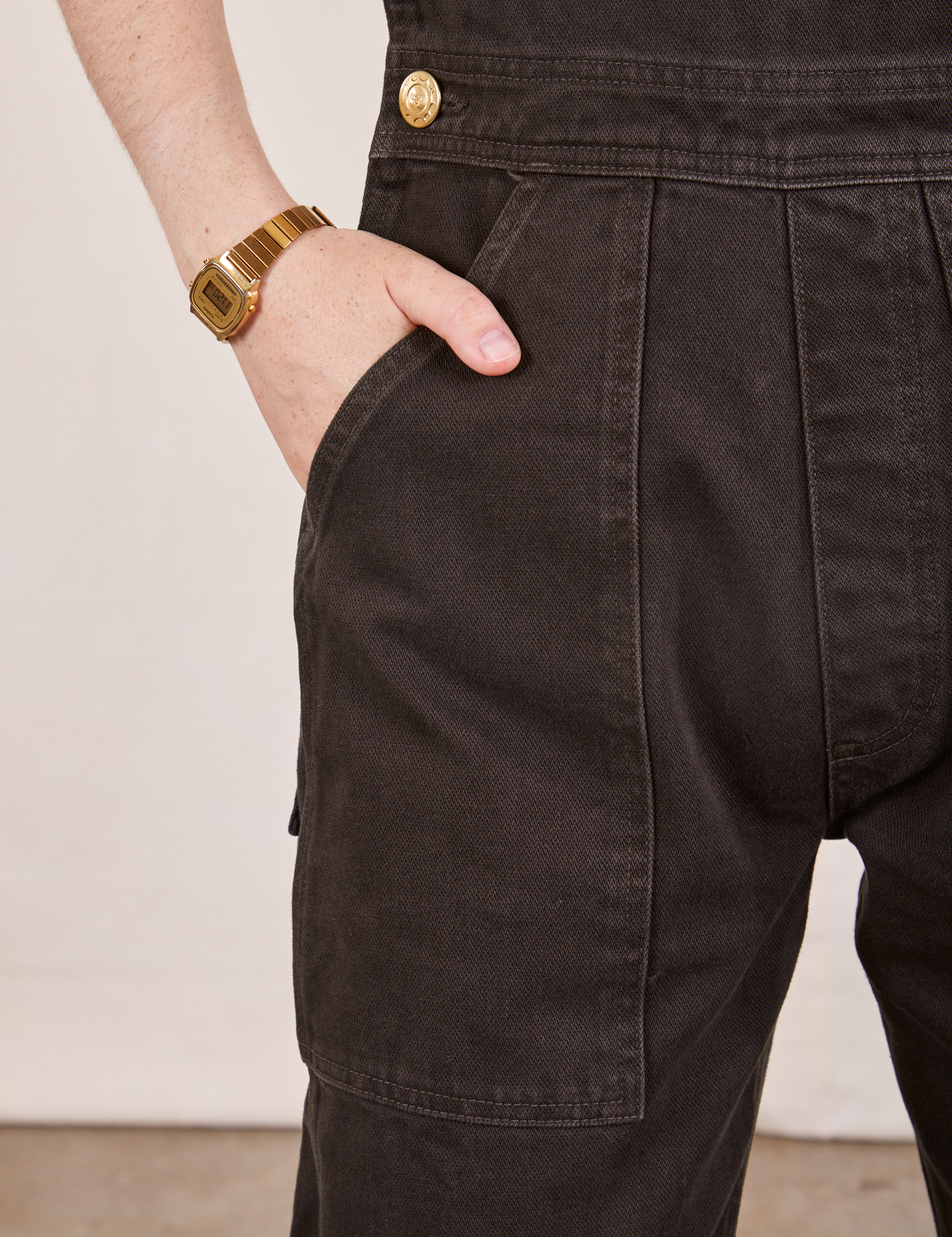 Front pocket close up of Original Overalls in Mono Espresso. Hana has her hand in the pocket.