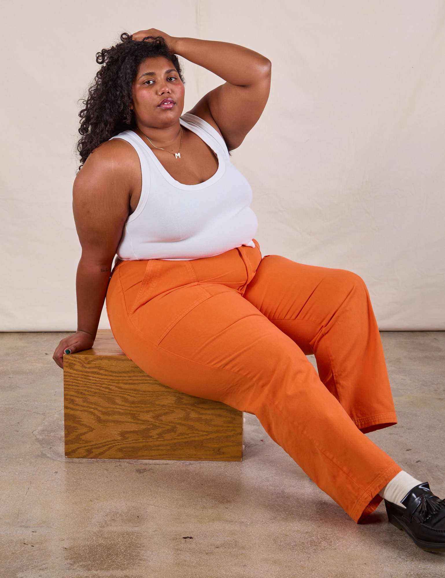 Work Pants in Construction Orange and Cropped Tank worn by Morgan sitting on a wooden box.