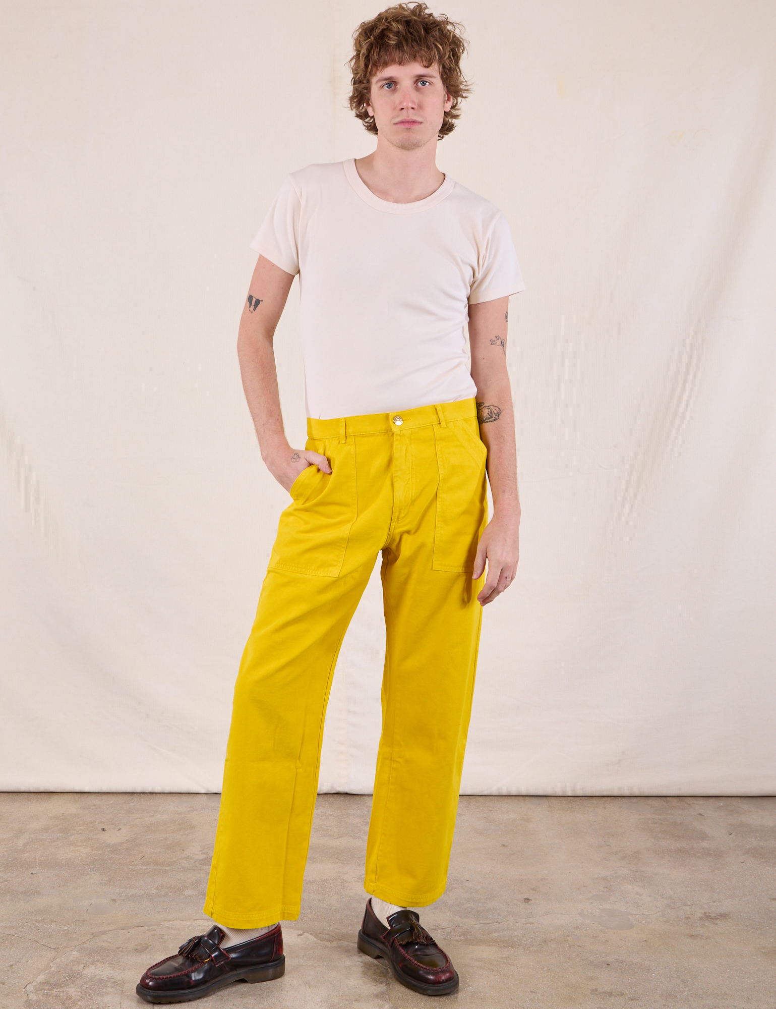 Quinn is 6’4” and wearing M Work Pants in Golden Yellow paired with a Burly Tee in Vintage Tee Off-White