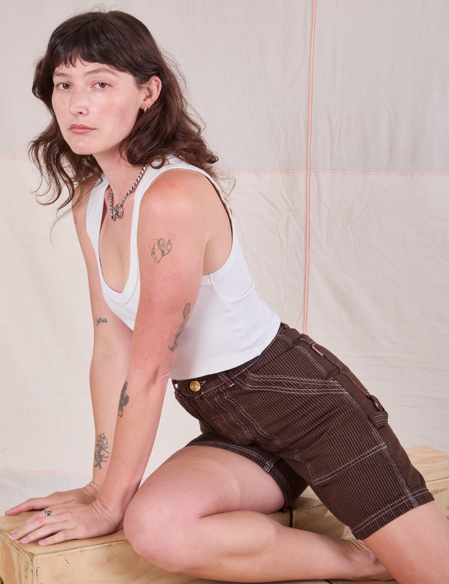 Alex is wearing Railroad Carpenter Shorts in Fudgesicle Brown and Cropped Tank in Vintage Tee Off-White