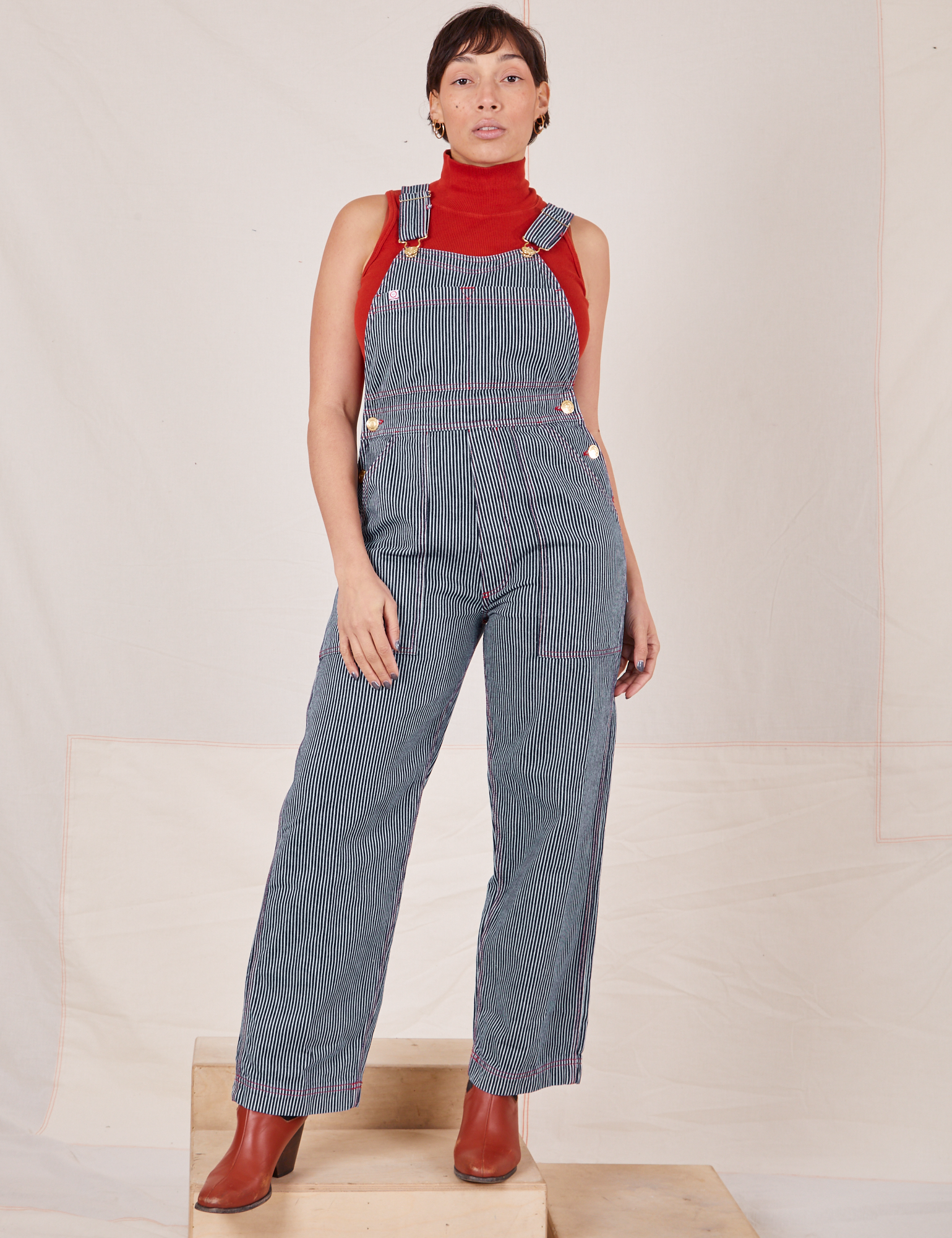 Tiara is 5&#39;4&quot; and wearing XS Railroad Stripe Denim Original Overalls paired with paprika Sleeveless Turtleneck