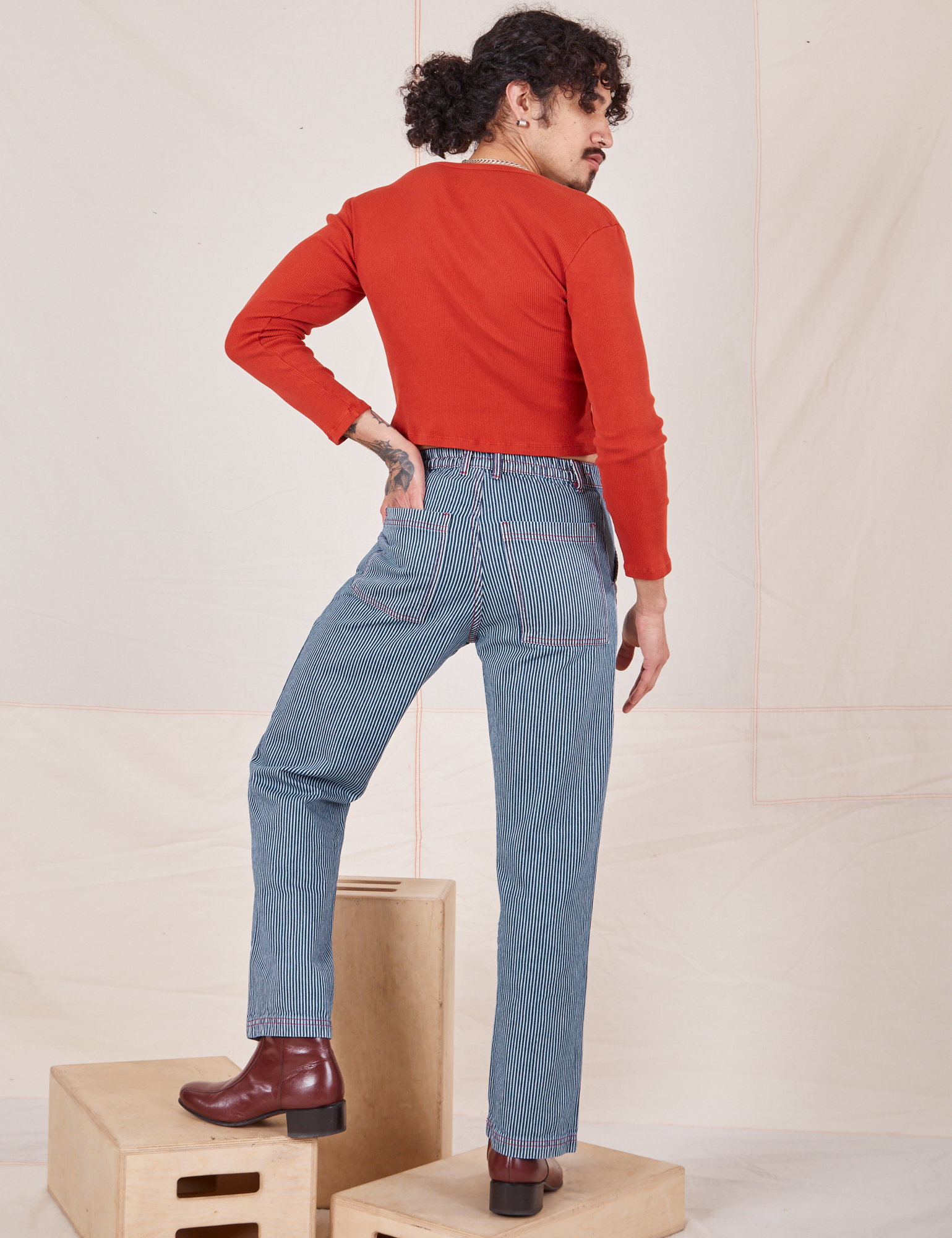 Back view of Railroad Stripe Denim Work Pants and paprika Long Sleeve V-Neck Tee worn by Jesse