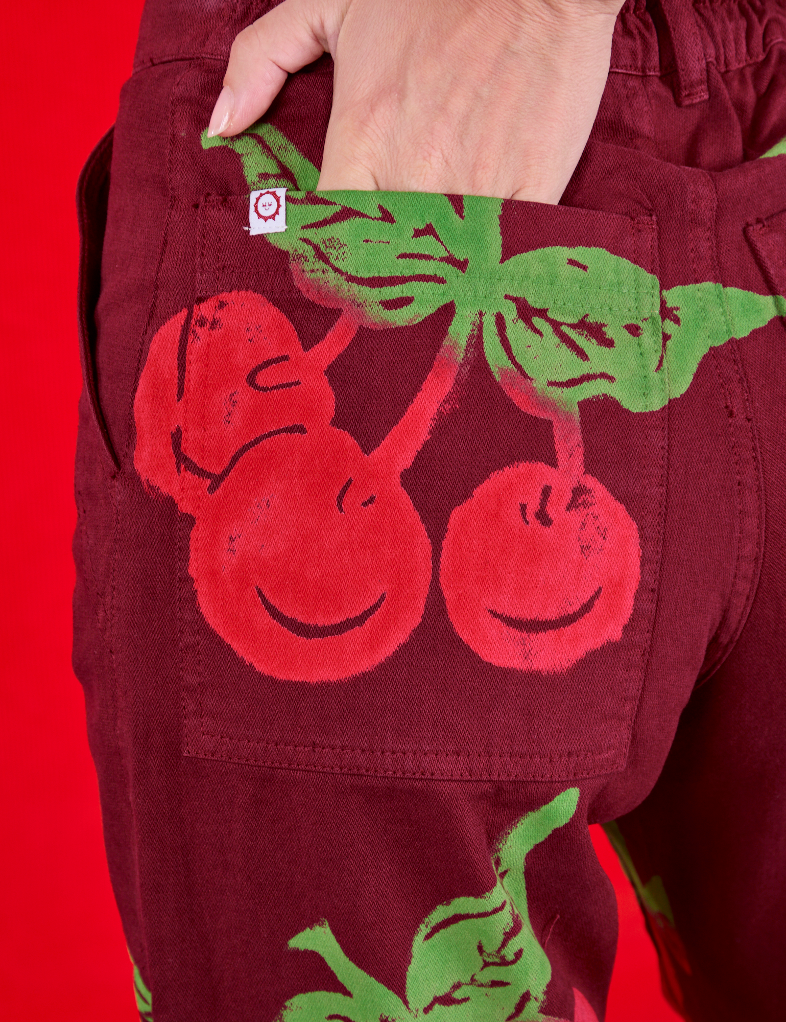 Close up of Madeline&#39;s hand in the back pocket of Paintstamped Work Pants in Cherry