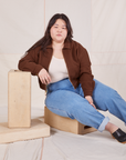 Ashley is sitting on a wooden crate wearing Ricky Jacket in Fudgesicle Brown, vintage off-white Tank Top and jeans