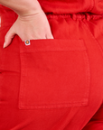 Short Sleeve Jumpsuit in Mustang Red back pocket close up. Lish has her hand in the pocket.