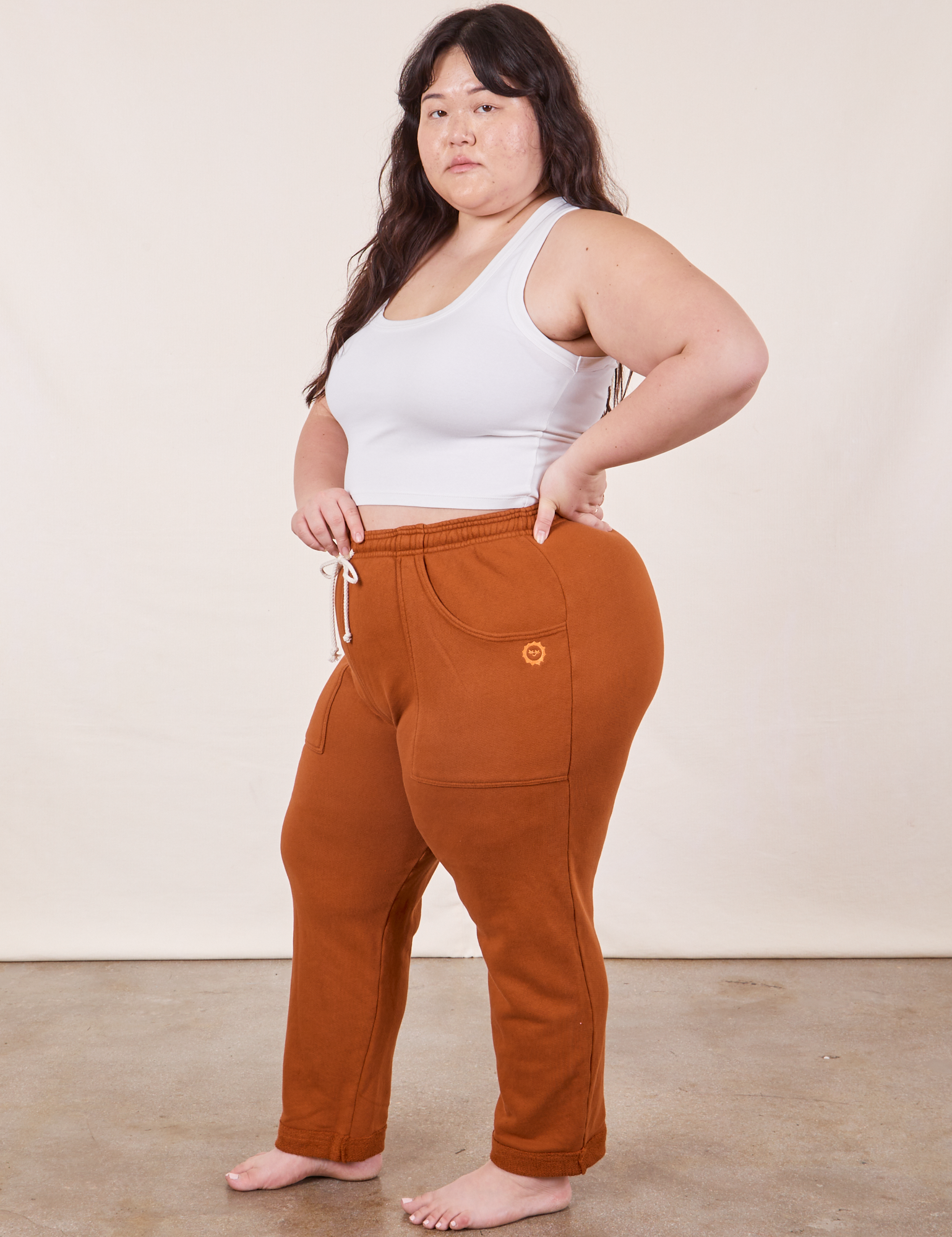 Side view of Cropped Rolled Cuff Sweatpants in Burnt Terracotta and vintage off-white Cropped Tank Top worn by Ashley