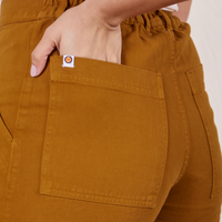 Classic Work Shorts in Spicy Mustard back pocket close up. Tiara has her hand in the back pocket.