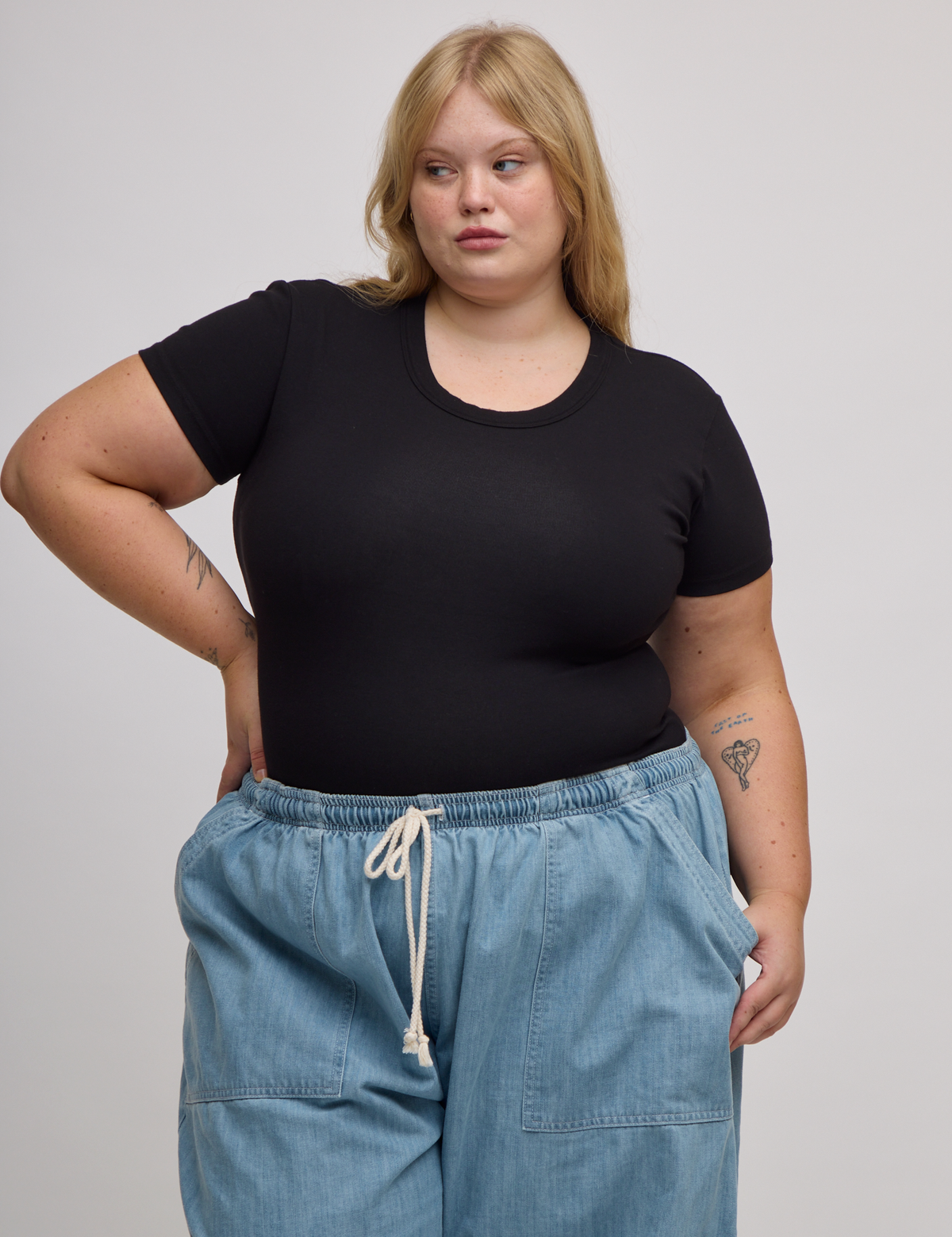 Juliet is wearing Baby Tee in Basic Black tucked into light wash denim drop pocket pants