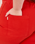 Bell Bottoms in Mustang Red back pocket close up. Marielena has her hand in the pocket.