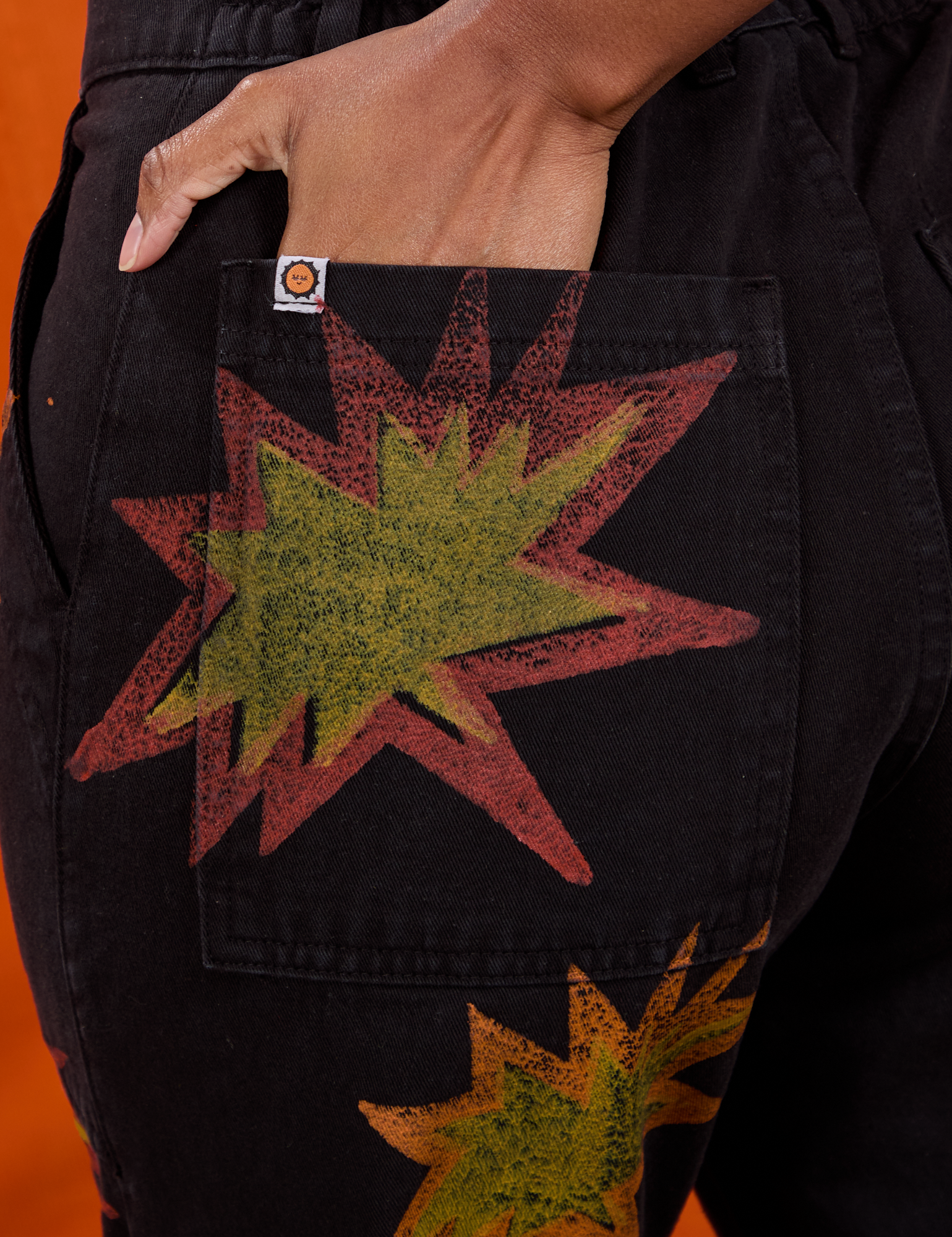 Close up of Kandia&#39;s hand in the back pocket of Paintstamped Work Pants in Explosion