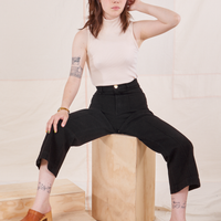 Hana is sitting on a wooden crate. She is wearing Heritage Westerns in Basic Black paired with vintage off-white Sleeveless Turtleneck