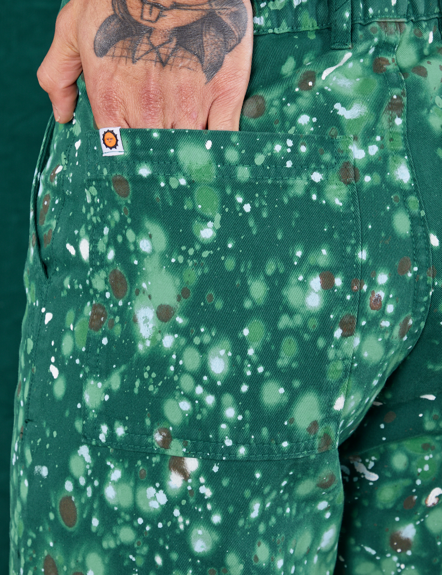 Marble Splatter Work Pants in Hunter Green back pocket close up. Jesse has their hand in the pocket.