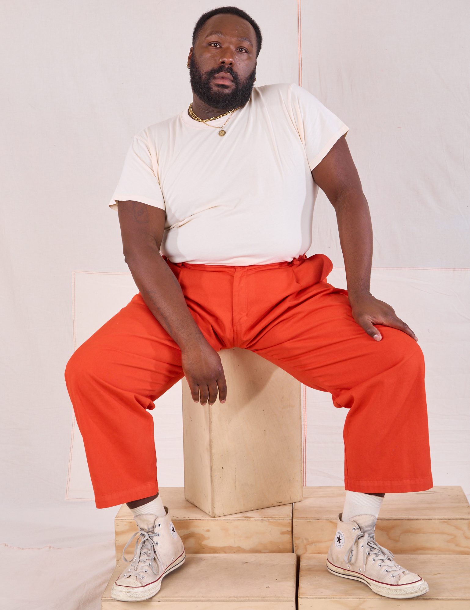 Elijah is wearing Mid-Rise Pleated Trousers in Chili Red and Organic Vintage Tee in vintage tee off-white