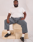 Elijah is wearing Mid-Rise Pleated Trousers in Slate Grey and Organic Vintage Tee in vintage tee off-white