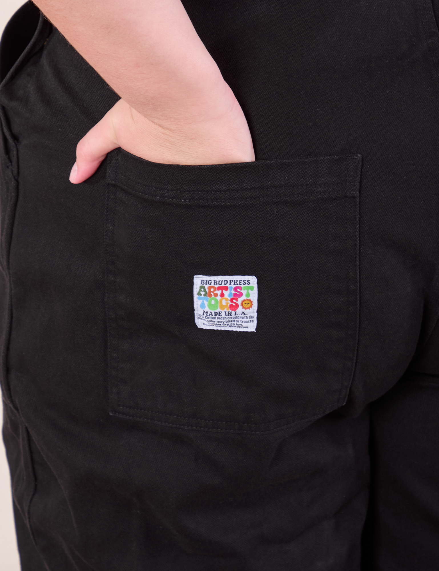 Original Overalls in Mono Black back pocket close up. Marielena has her hand in the pocket.