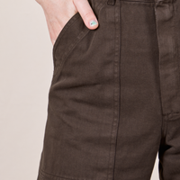 Front pocket close up of Petite Short Sleeve Jumpsuit in Espresso Brown. Worn by Hana with her hand in the pocket.