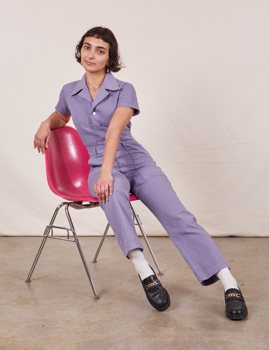 Soraya is sitting in a pink chair wearing Petite Short Sleeve Jumpsuit in Faded Grape