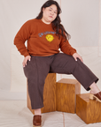 Ashley is sitting on a wooden crate wearing Bill Ogden's Sun Baby Crew and espresso brown Western Pants